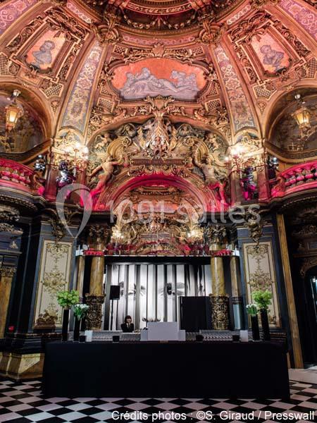 Intérieur d'une salle richement décorée avec des fresques, moulures dorées et un plafond voûté orné.