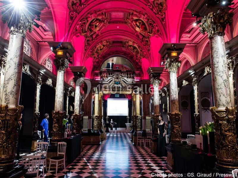 Salle ornée de colonnes et de voûtes richement décorées, éclairée par des lumières roses.