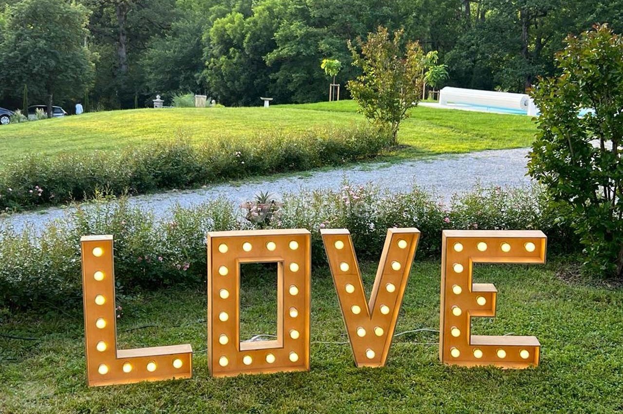 Lettres lumineuses formant le mot ’LOVE’ installées sur une pelouse, avec un parc verdoyant en arrière-plan.