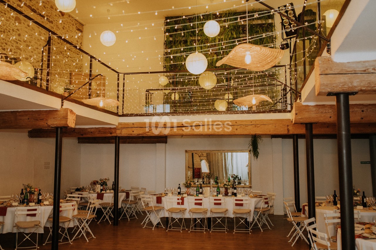 Salle de réception décorée avec des guirlandes lumineuses, des tables dressées et un mur végétal en arrière-plan.