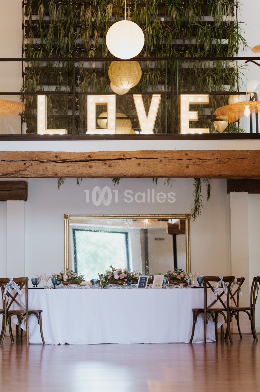 Salle décorée pour un événement avec une table ornée de fleurs et le mot ’LOVE’ illuminé en arrière-plan.