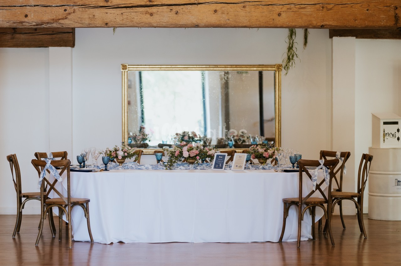 Table élégamment dressée avec des fleurs et des verres, entourée de chaises en bois, devant un grand miroir doré.