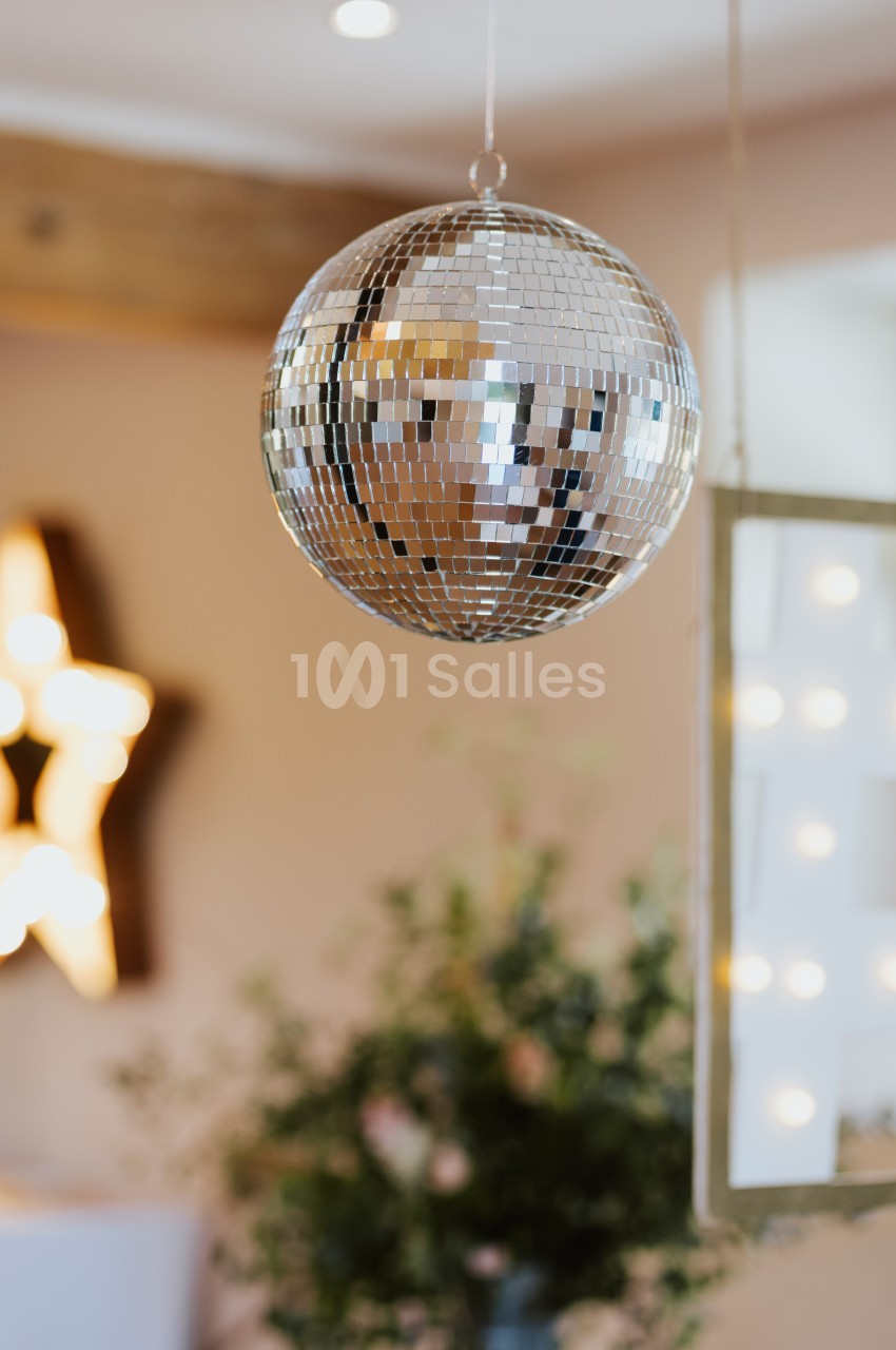Boule à facettes suspendue dans une pièce lumineuse avec des décorations floues en arrière-plan.