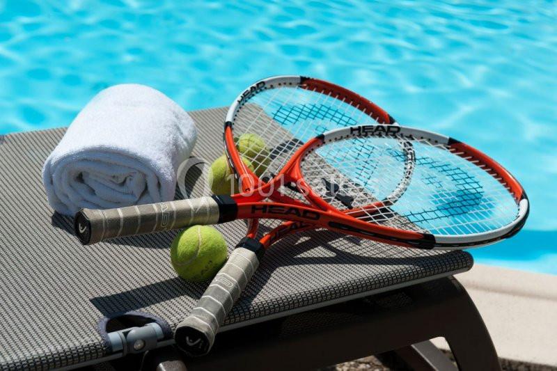 Deux raquettes de tennis, trois balles et une serviette blanche posées sur un transat près d'une piscine.