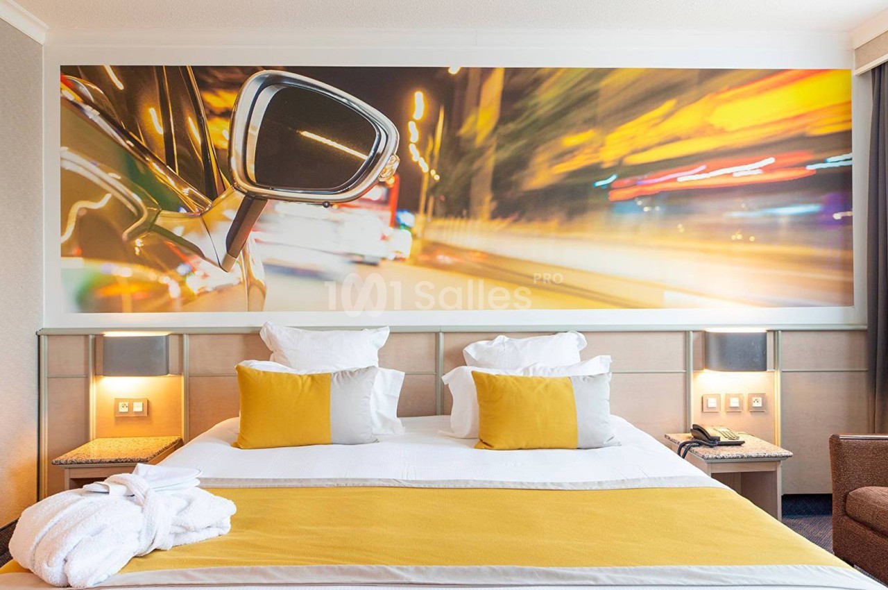 Lit double avec coussins jaunes dans une chambre moderne, décorée d'une grande photo murale de voiture en mouvement.