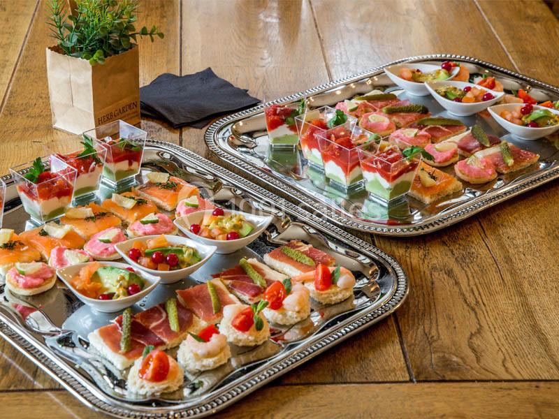 Plateaux de canapés variés avec légumes, saumon, jambon et verrines colorées, disposés sur une table en bois.