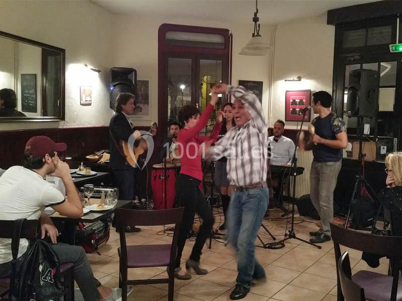 Des personnes dansent au centre d'un café animé, avec un groupe de musiciens jouant en arrière-plan.