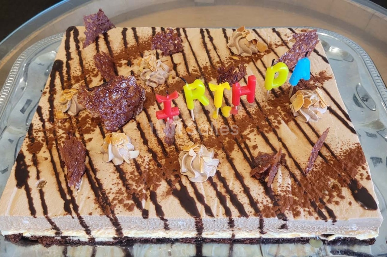 Gâteau rectangulaire décoré de chocolat, crème et lettres colorées formant ’BIRTHDAY’.