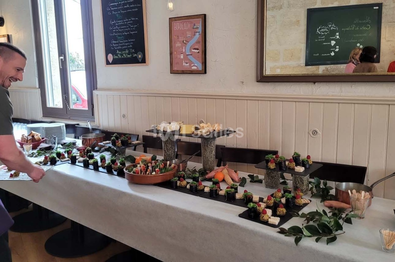 Table garnie de plats variés et colorés dans un restaurant, avec un homme souriant ajustant la présentation.