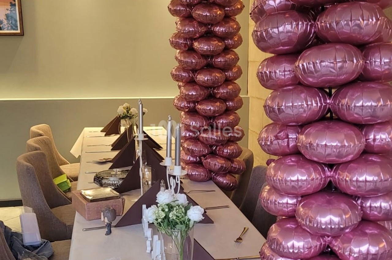 Table décorée avec des bougies, des fleurs blanches et des colonnes de ballons roses dans une salle élégante.