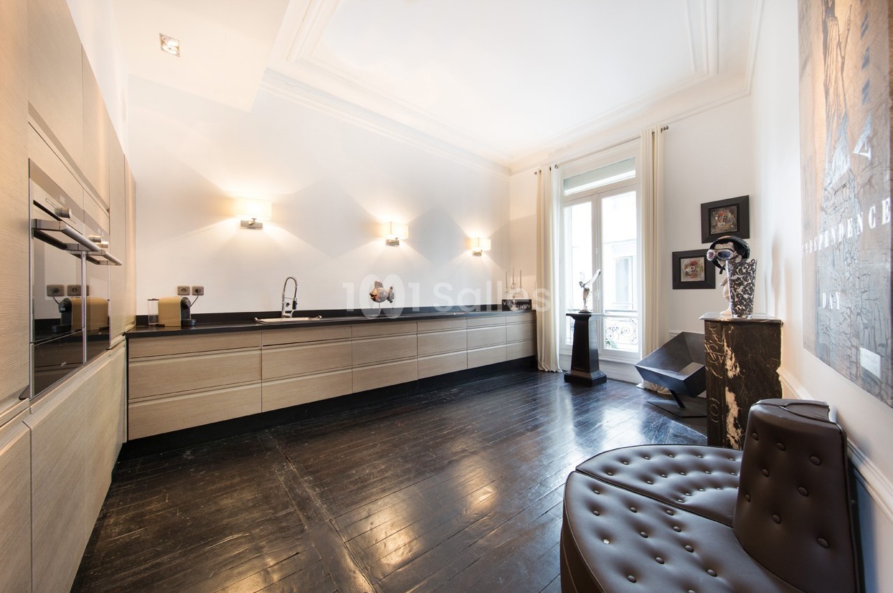Cuisine moderne avec meubles en bois clair, plan de travail noir, sol en parquet foncé et grande fenêtre lumineuse.