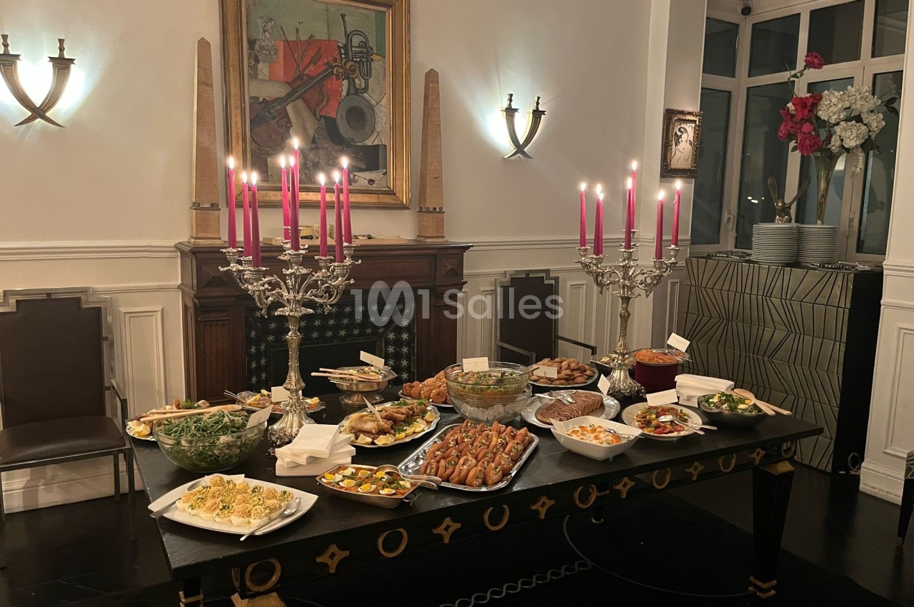 Table dressée avec divers plats et bougeoirs ornés de bougies roses, dans une salle élégante avec cheminée et décorations…