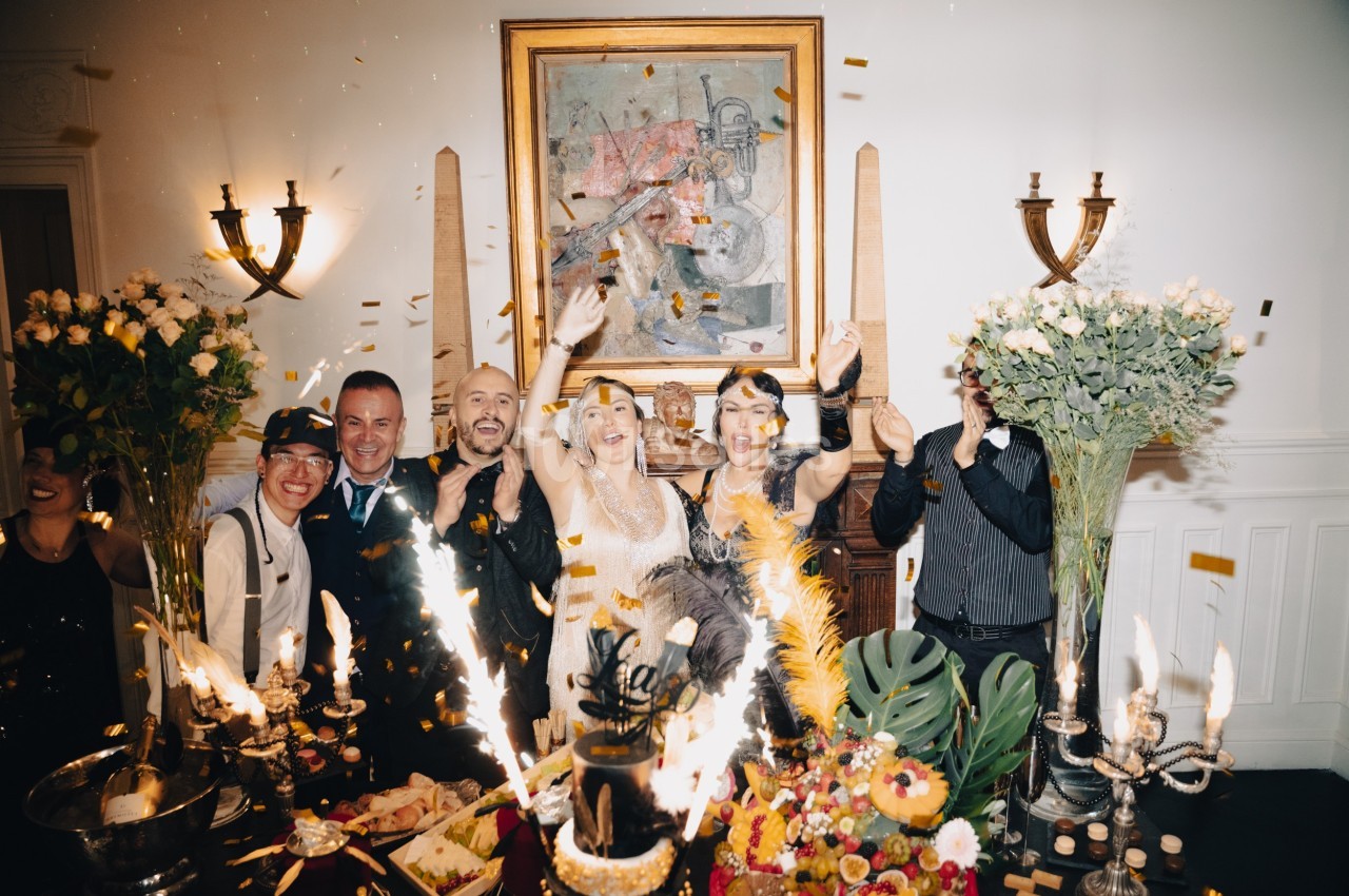 Des personnes célèbrent joyeusement dans une salle décorée, entourées de fleurs, de bougies et de confettis.