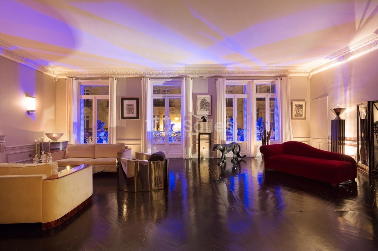 Salon spacieux avec parquet sombre, canapés, fauteuils design, éclairage tamisé et grandes fenêtres donnant sur l'extérieur.