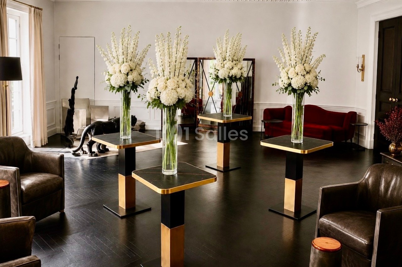 Quatre arrangements floraux blancs sur des tables modernes dans un salon élégant avec des fauteuils et un canapé rouge.