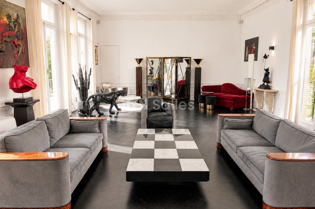 Salon spacieux avec mobilier design, canapé gris, table basse damier, sculptures et miroirs décoratifs.