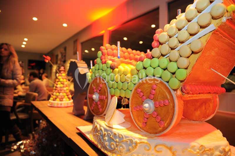 Pièce montée en forme de carrosse décorée de macarons colorés, exposée sur une table dans un intérieur éclairé.