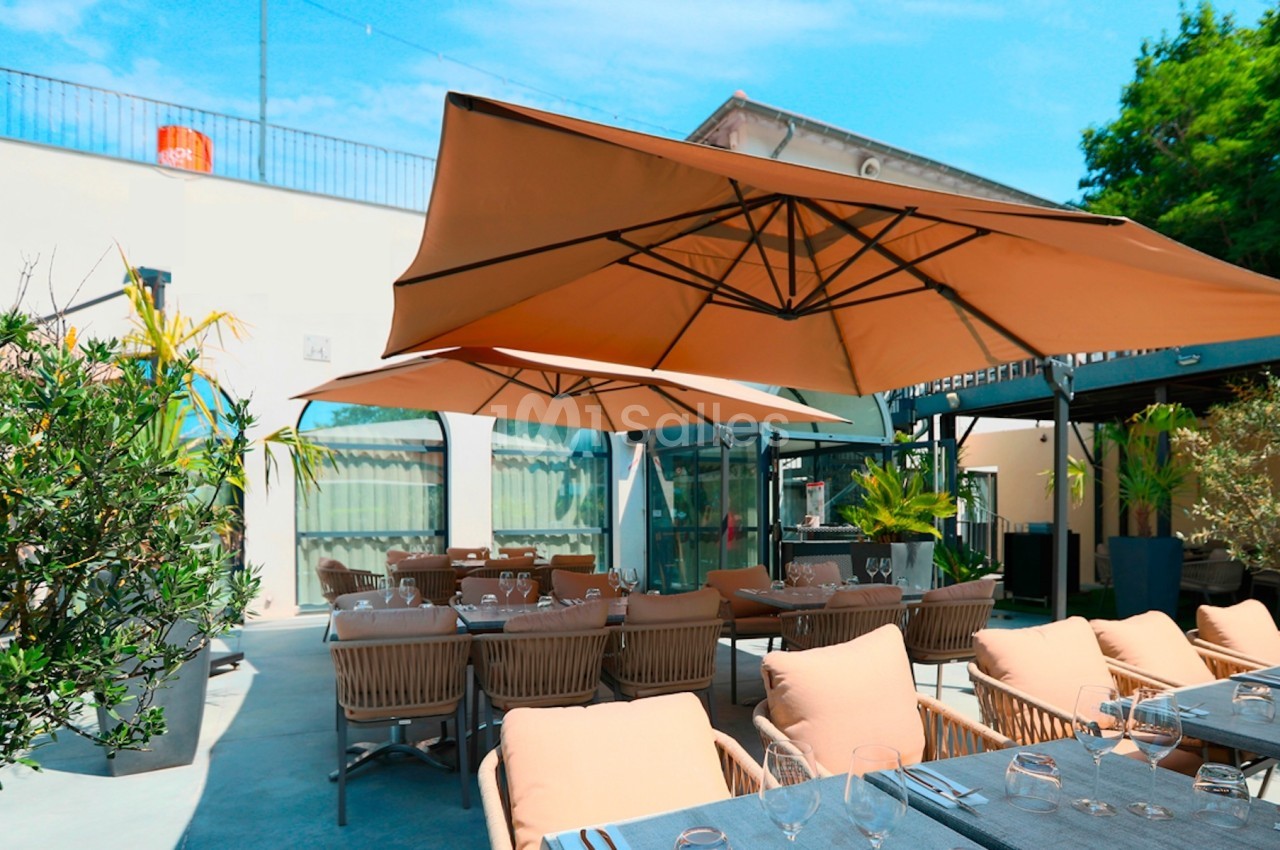 Terrasse extérieure avec tables dressées, chaises en rotin et grands parasols beige sous un ciel bleu.