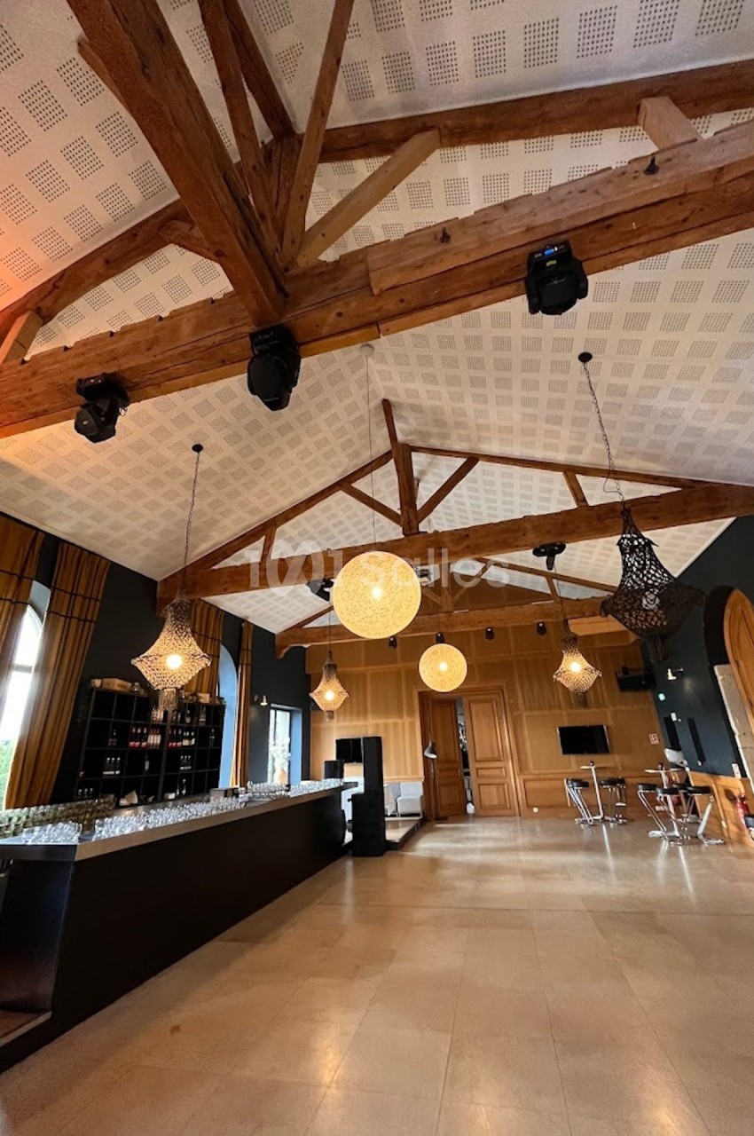 Plafond avec poutres en bois apparentes dans une salle moderne, équipée d'un bar et de luminaires suspendus.