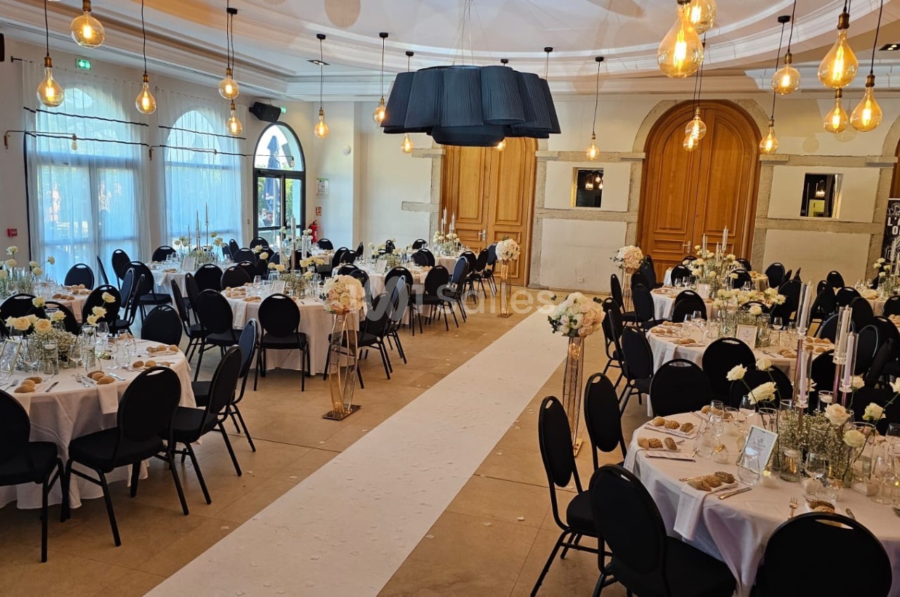 Salle de réception élégamment décorée avec des tables rondes, des chaises noires et des arrangements floraux blancs.