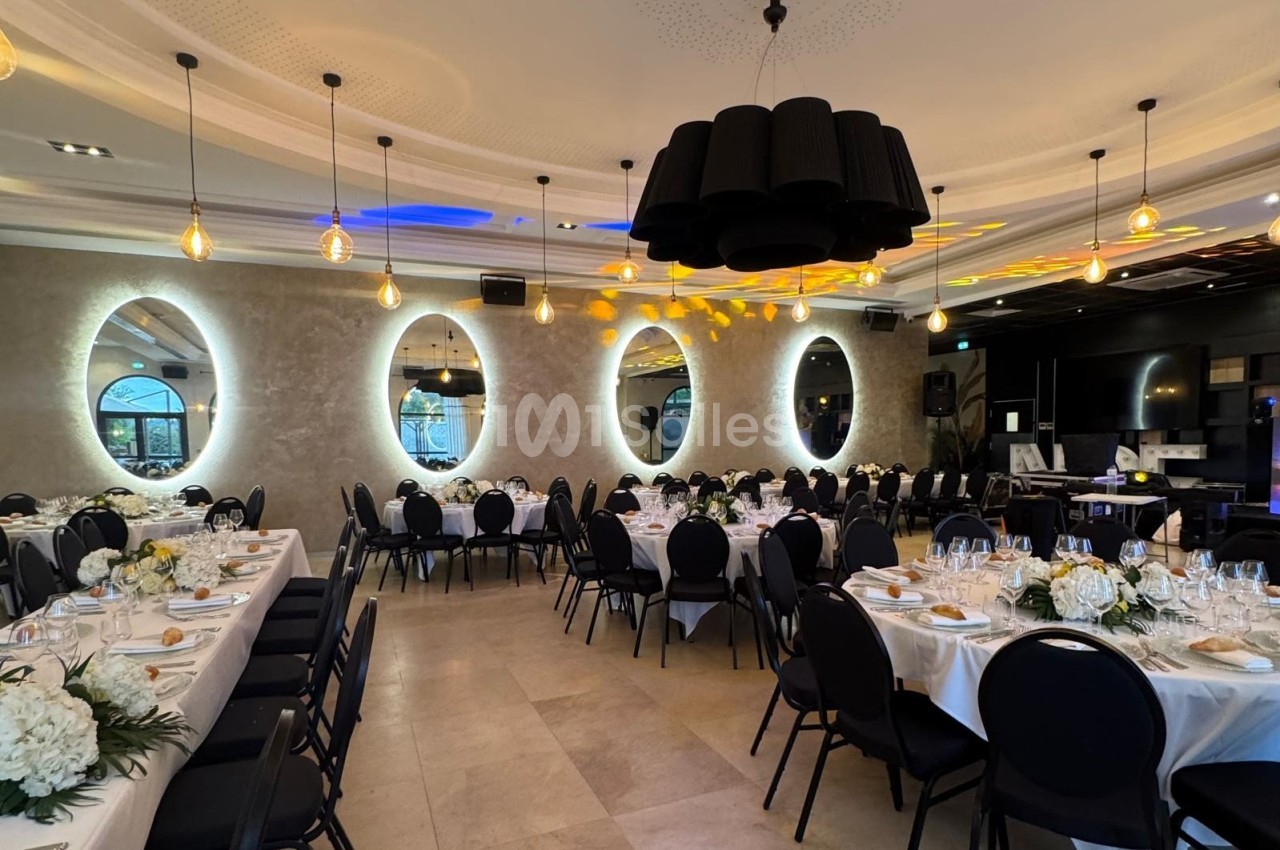 Salle de réception élégante avec tables dressées, miroirs ovales éclairés et lustres modernes au plafond.