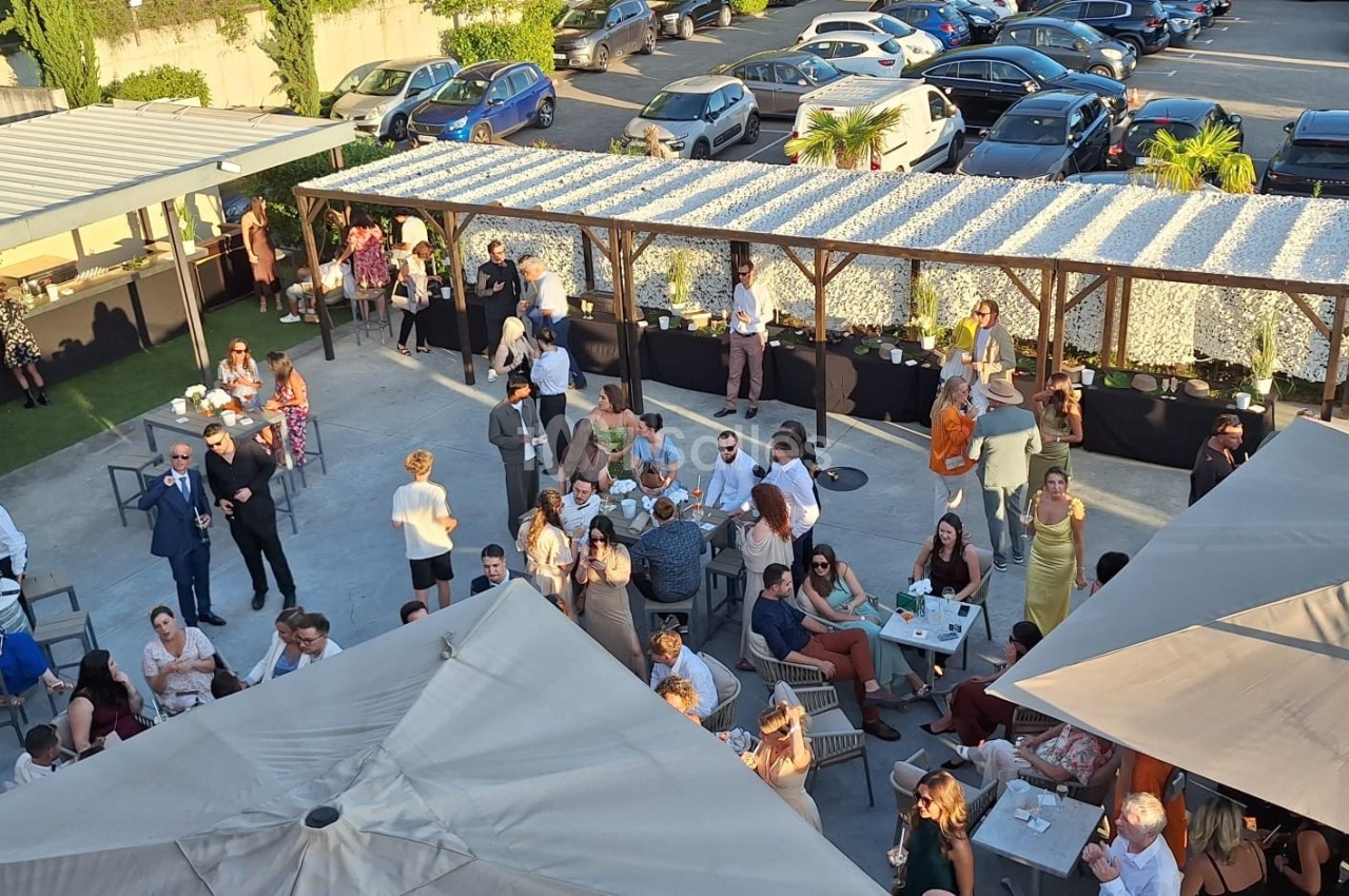 Vue aérienne d'une terrasse animée avec des groupes de personnes discutant et profitant d'un événement en plein air.