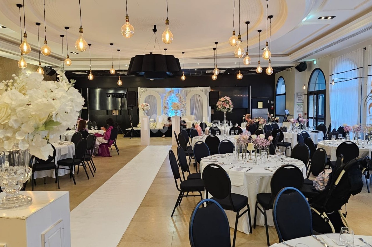 Salle de réception élégante avec tables dressées, décor floral et éclairage suspendu dans une ambiance lumineuse.