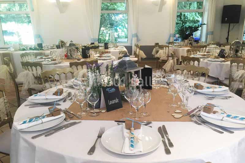 Salle de réception décorée avec des tables rondes dressées, ornées de lanternes, fleurs et marque-places.