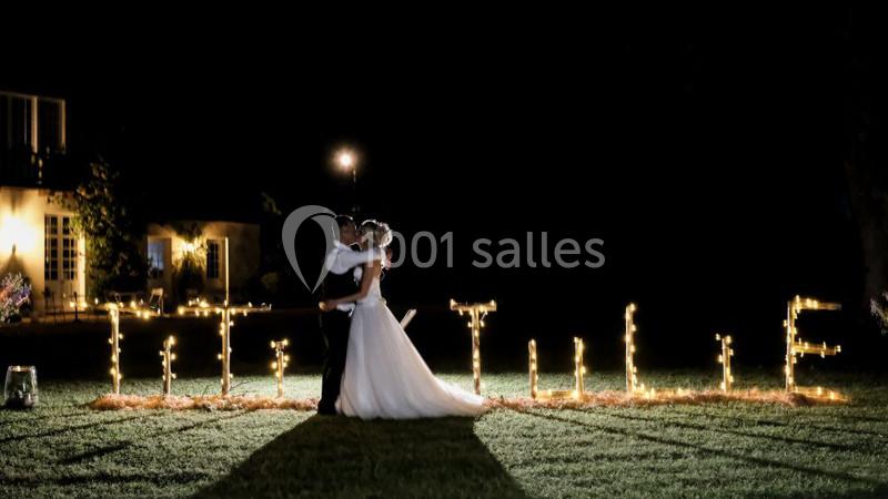 Un couple de mariés s'embrasse devant des lettres lumineuses formant un mot, dans un jardin éclairé de nuit.