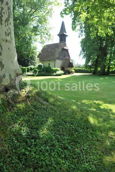 Petite chapelle en bois entourée de verdure, située dans un parc arboré sous un ciel clair.