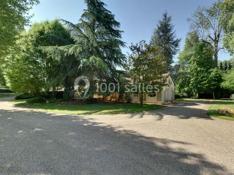 Maison entourée d'arbres et de végétation, avec une allée en gravier au premier plan sous un ciel dégagé.