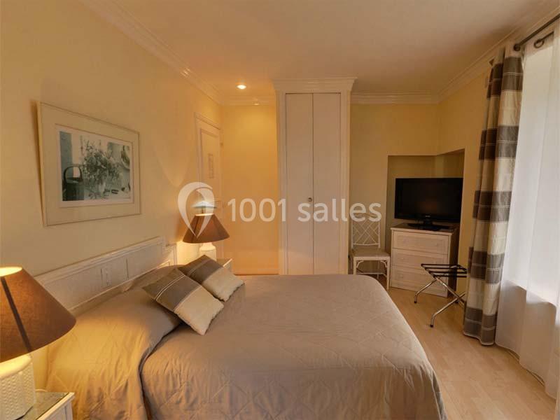 Chambre lumineuse avec lit double, lampes de chevet, armoire blanche, télévision et rideaux à motifs.