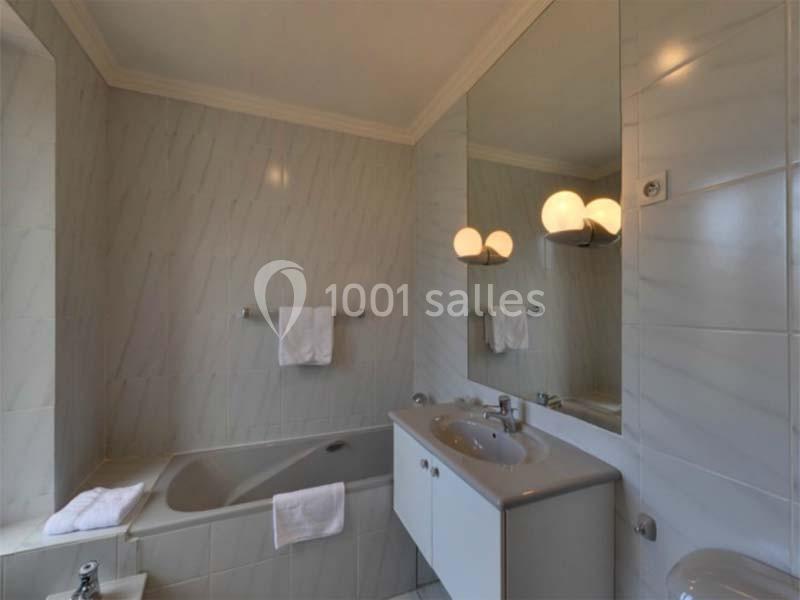 Salle de bain avec baignoire, lavabo double, miroir éclairé et murs carrelés dans des tons clairs.