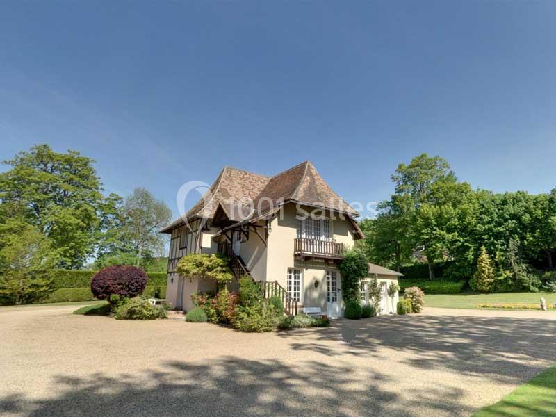 Maison traditionnelle avec toit en pente, entourée d'arbres et d'un jardin, sous un ciel dégagé.
