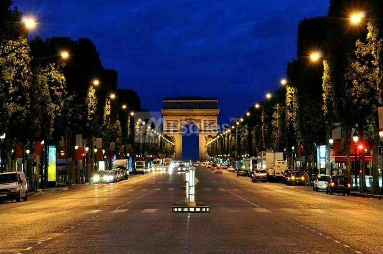 Vue nocturne de l'Avenue des Champs-Élysées illuminée, avec l'Arc de Triomphe en arrière-plan.