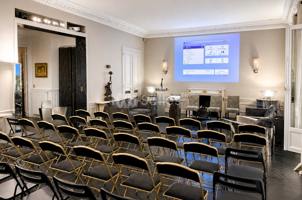 Salle de réunion élégante avec chaises alignées, écran de projection allumé et décoration intérieure raffinée.