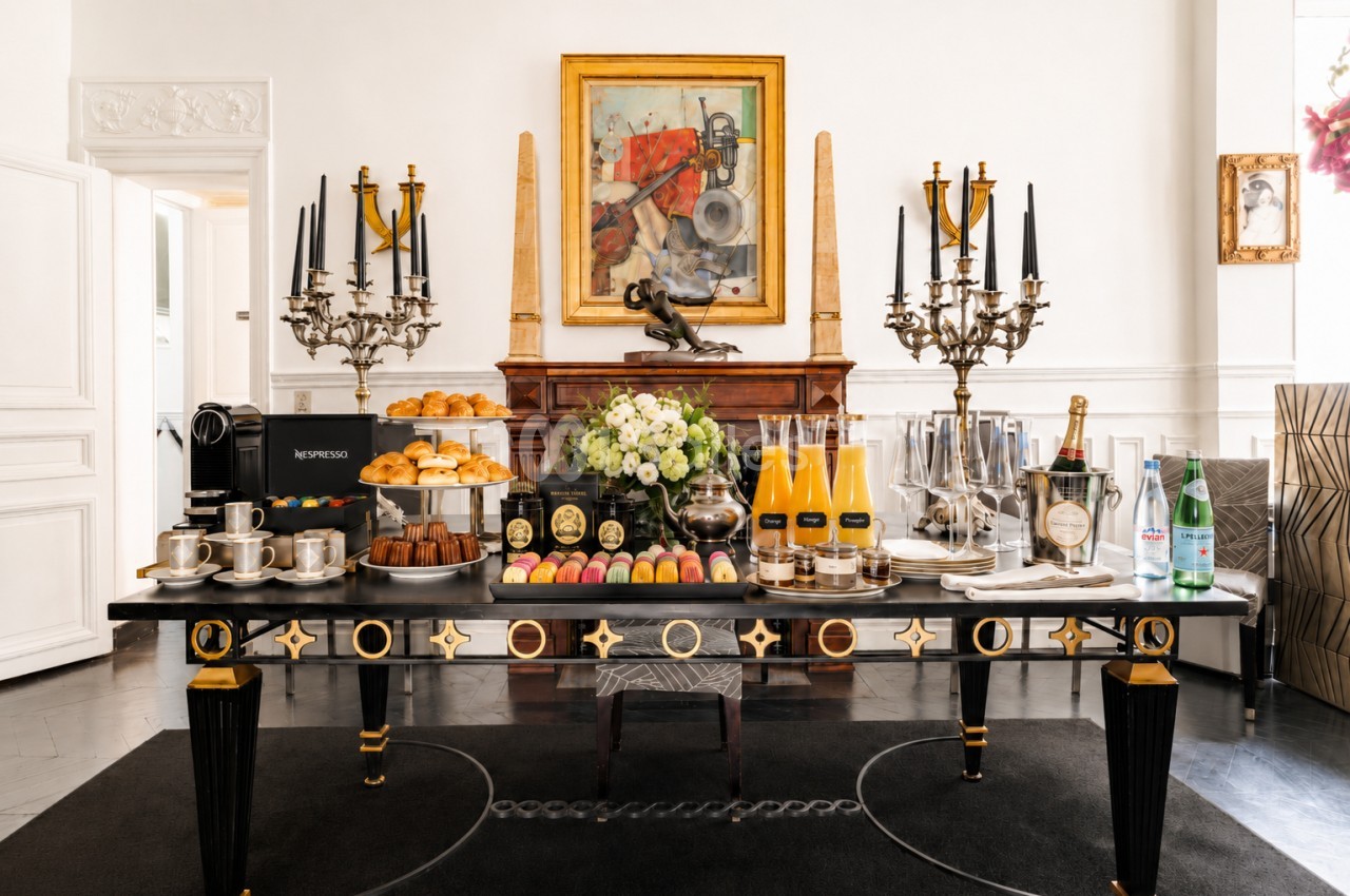 Table élégante dressée avec pâtisseries, macarons, jus d'orange, café et décorations raffinées dans un intérieur chic.