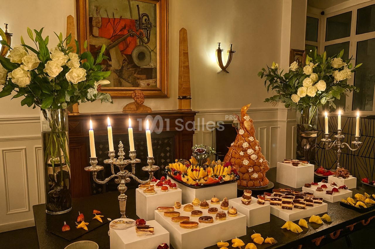 Table décorée avec des chandeliers, fleurs blanches et desserts variés, dont une pièce montée, dans une salle élégante.
