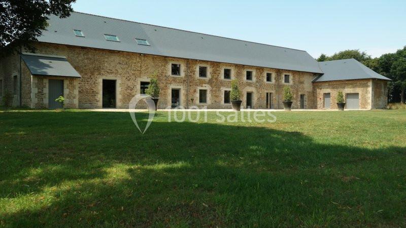Bâtiment en pierre avec toit en ardoise, grandes fenêtres et pots de plantes, entouré d'une pelouse verte.