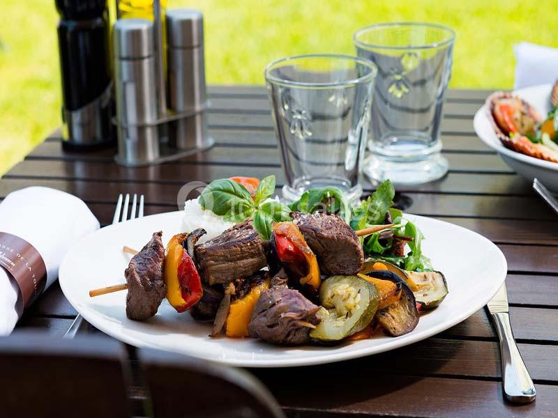 Assiette de brochettes de viande grillée avec légumes, accompagnée de salade verte et servie sur une table en extérieur.