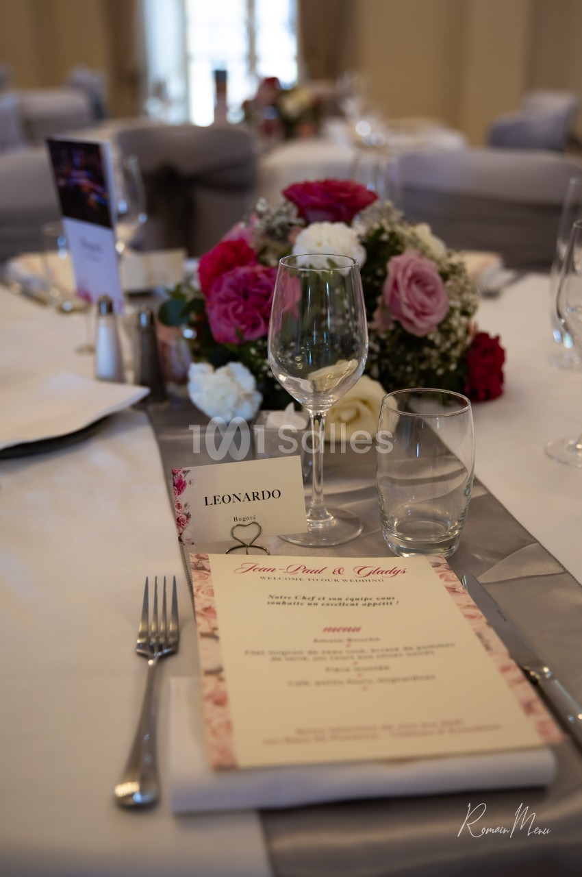 Table de réception élégamment dressée avec menu, verres, et centre de table floral composé de roses rouges et blanches.