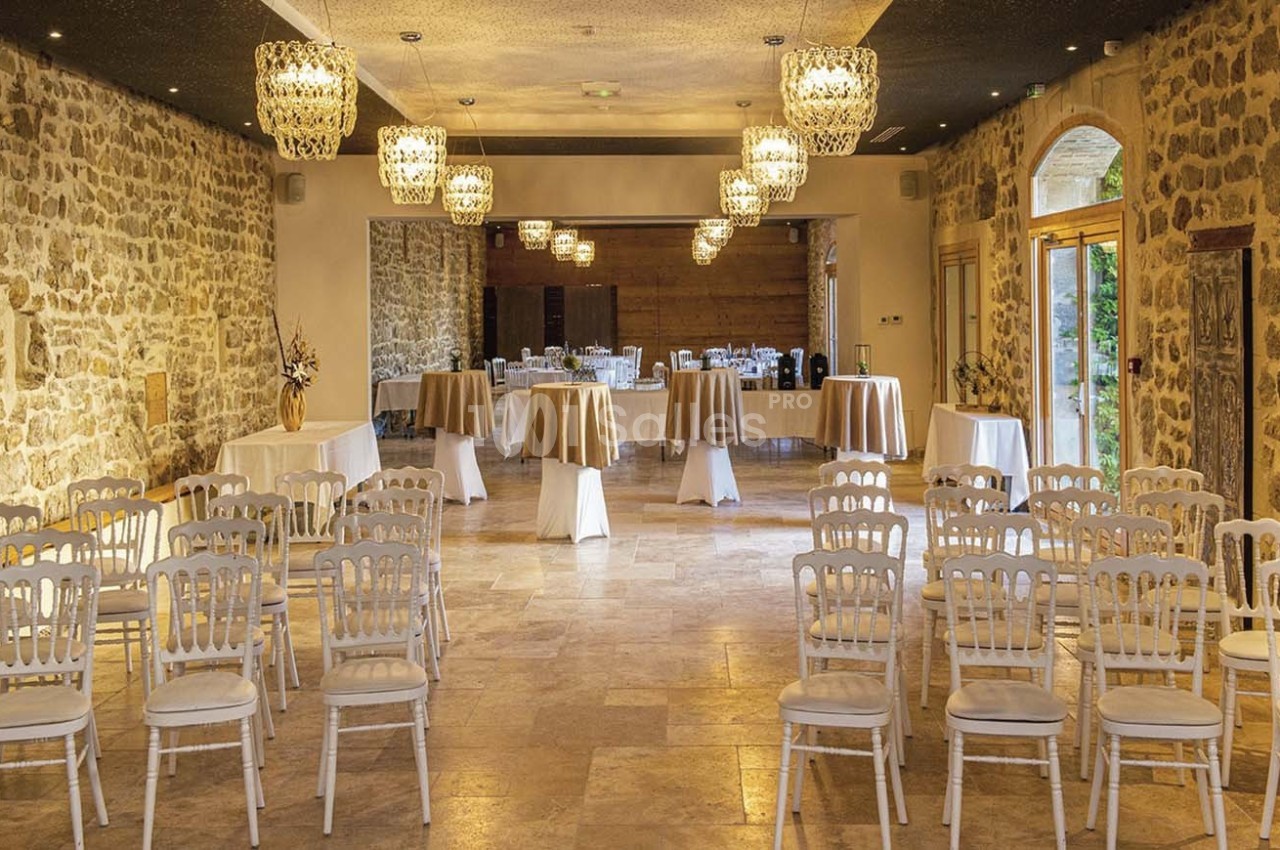 Salle de réception en pierre avec chaises alignées, tables dressées et lustres suspendus.