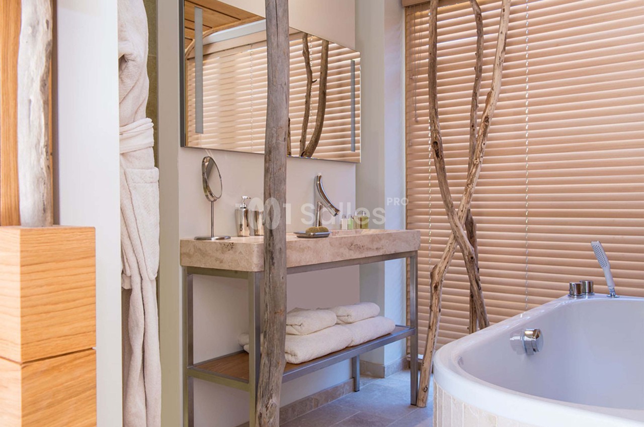 Salle de bain moderne avec lavabo en pierre, baignoire, miroir, serviettes pliées et stores en bois.
