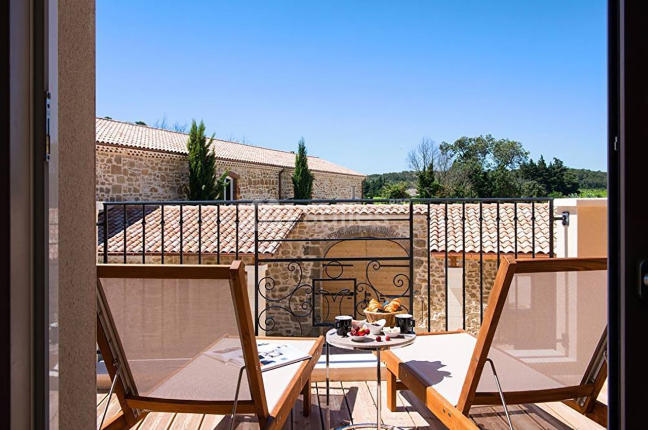 Deux chaises longues en bois sur une terrasse avec vue sur des bâtiments en pierre et un ciel bleu dégagé.