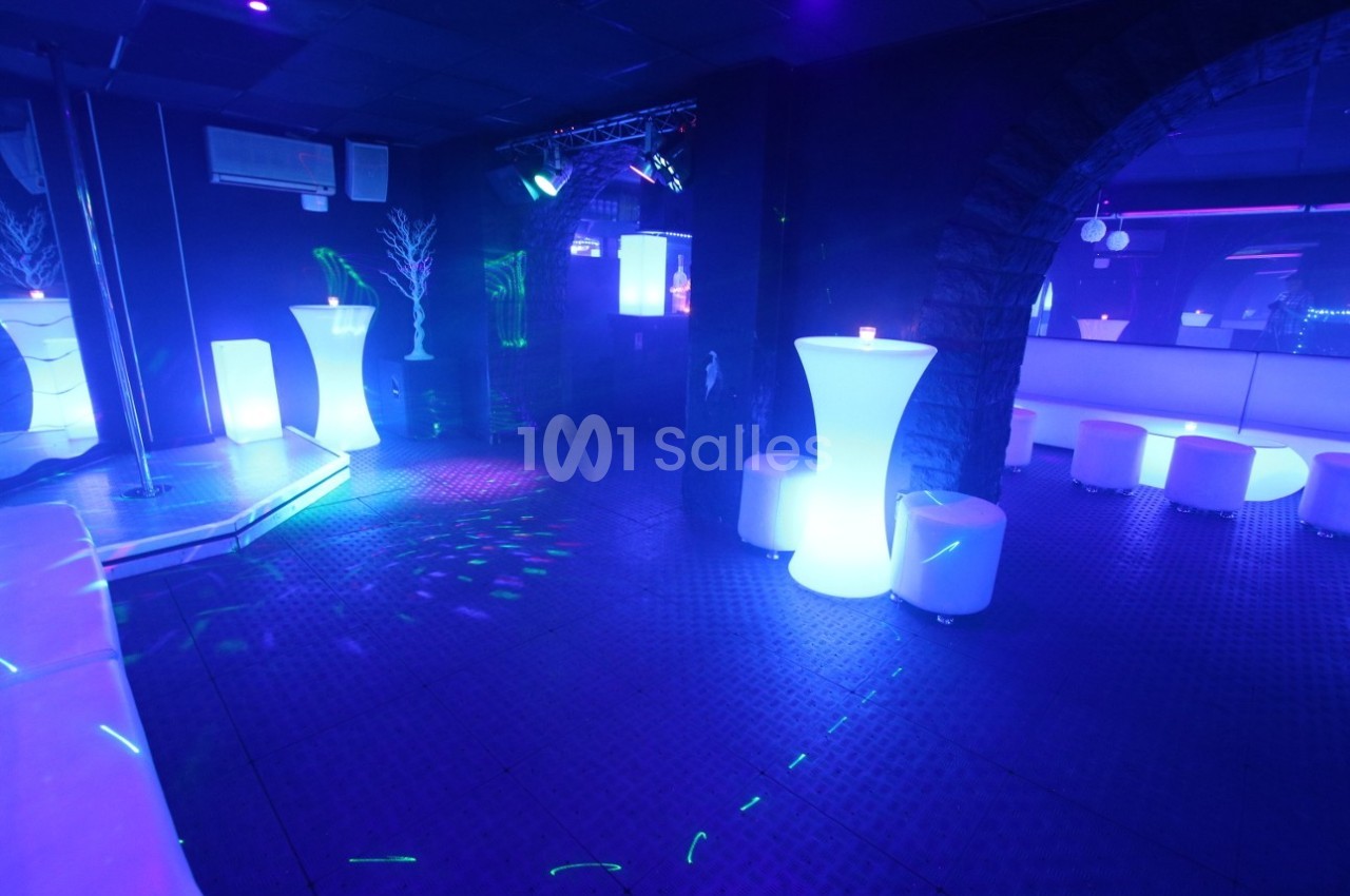 Salle de réception avec éclairage bleu, tables hautes lumineuses et sièges blancs dans une ambiance nocturne.