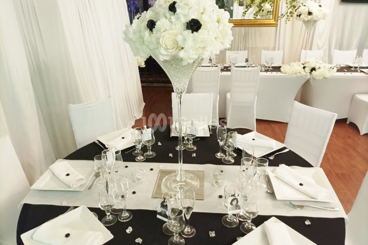 Table élégamment dressée avec nappes noires et blanches, décorée d'un grand bouquet de fleurs blanches et noires.