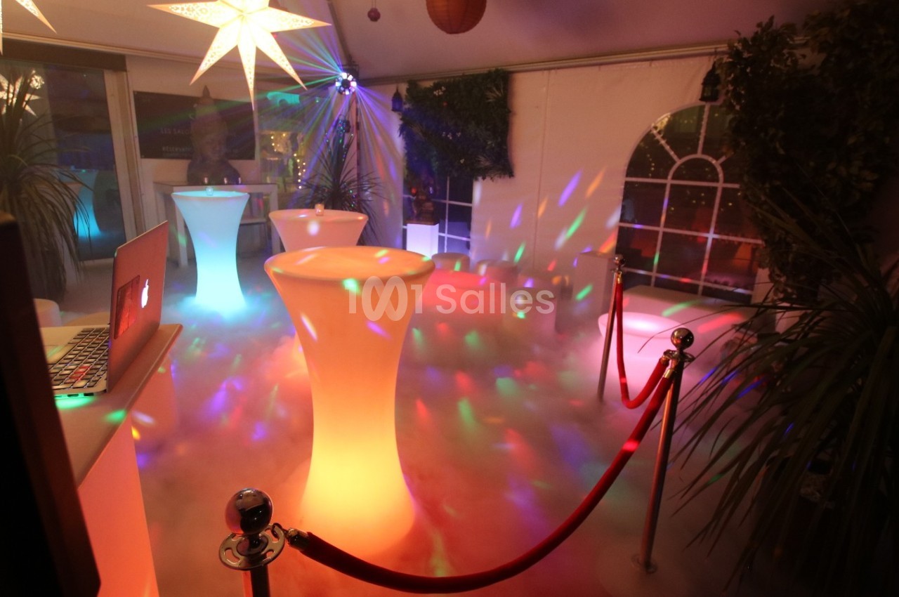 Salle décorée avec des tables lumineuses, éclairages colorés, plantes et effets de fumée au sol.