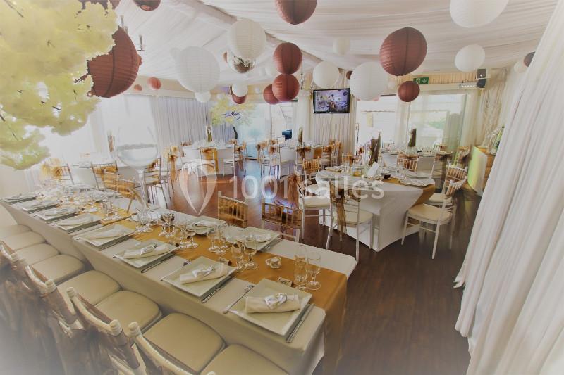 Salle de réception décorée avec des lanternes suspendues, des tables dressées et des chaises en bois clair.