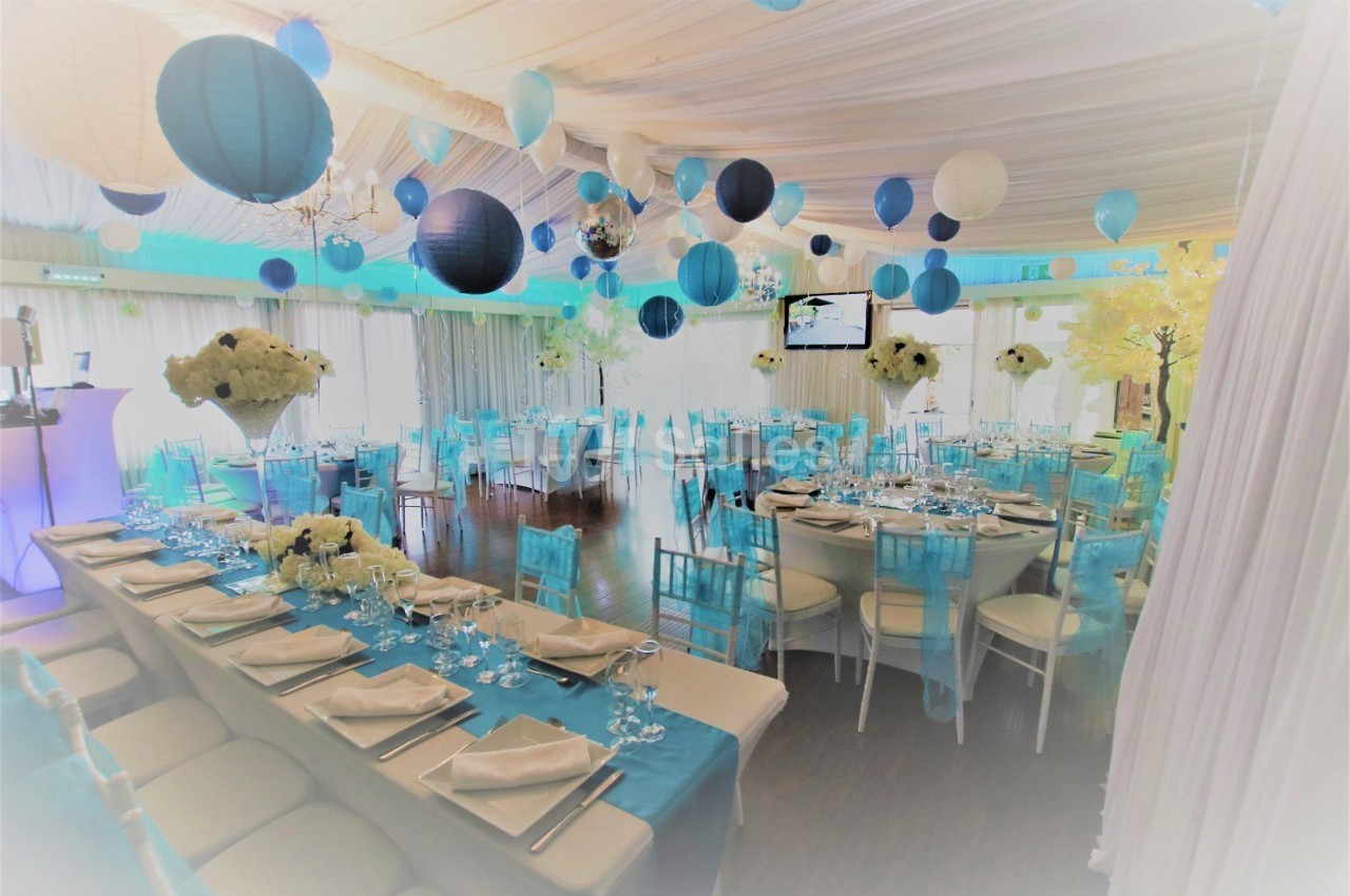 Salle de réception décorée avec des lanternes bleues et blanches, tables dressées et chaises assorties.