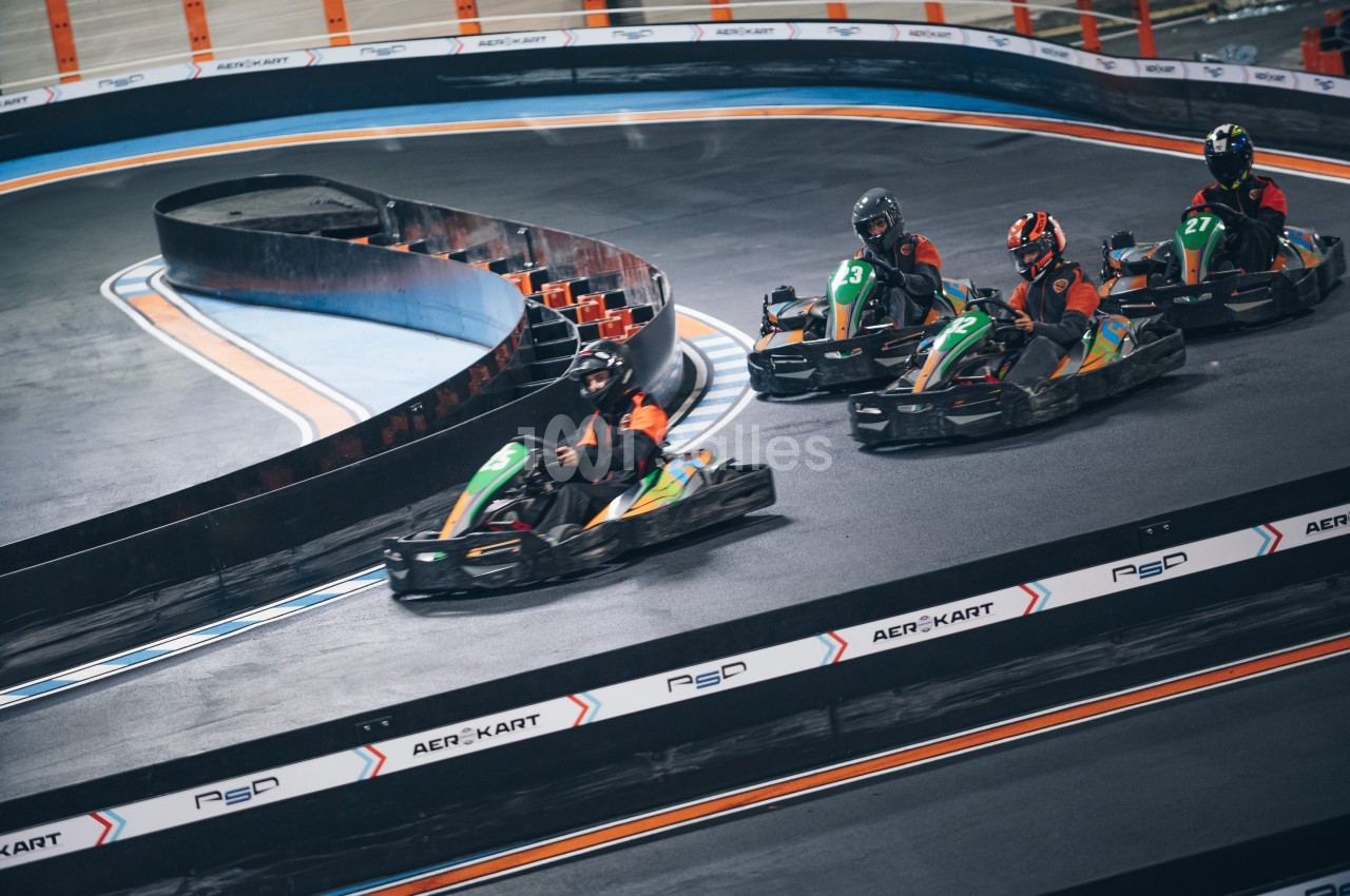 Quatre personnes conduisent des karts sur une piste intérieure avec des virages serrés.